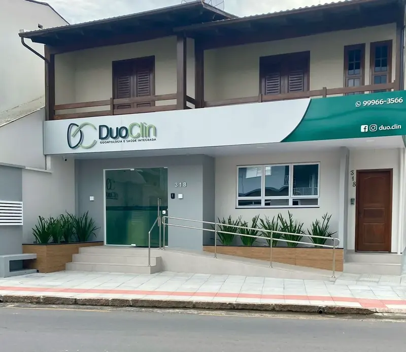 Fachada da DuoClin, prédio branco com a faixa verde e o logo da clínica