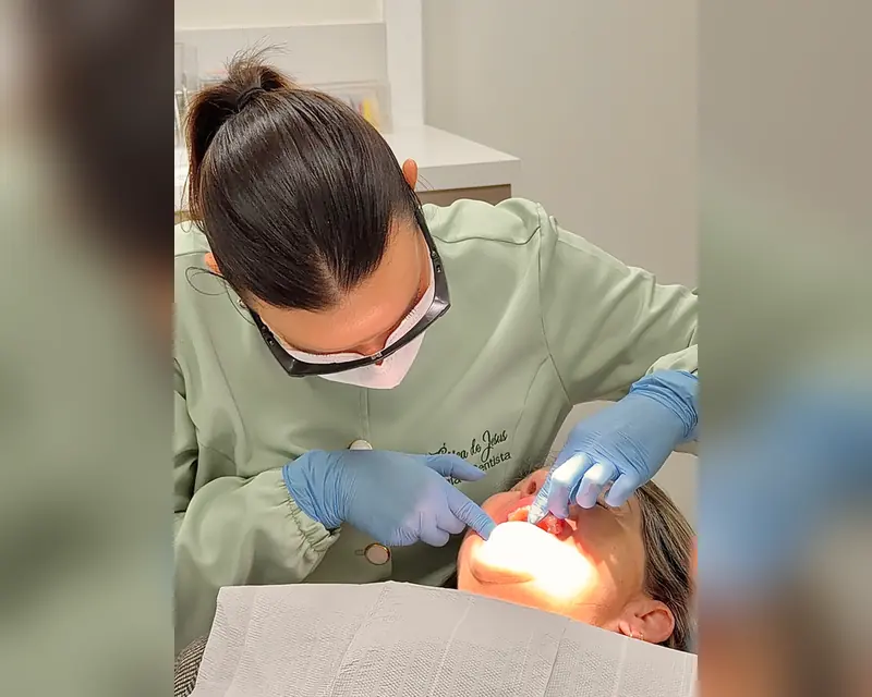 Dra. Érica examinando a boca de uma paciente na cadeira, de máscara e óculos